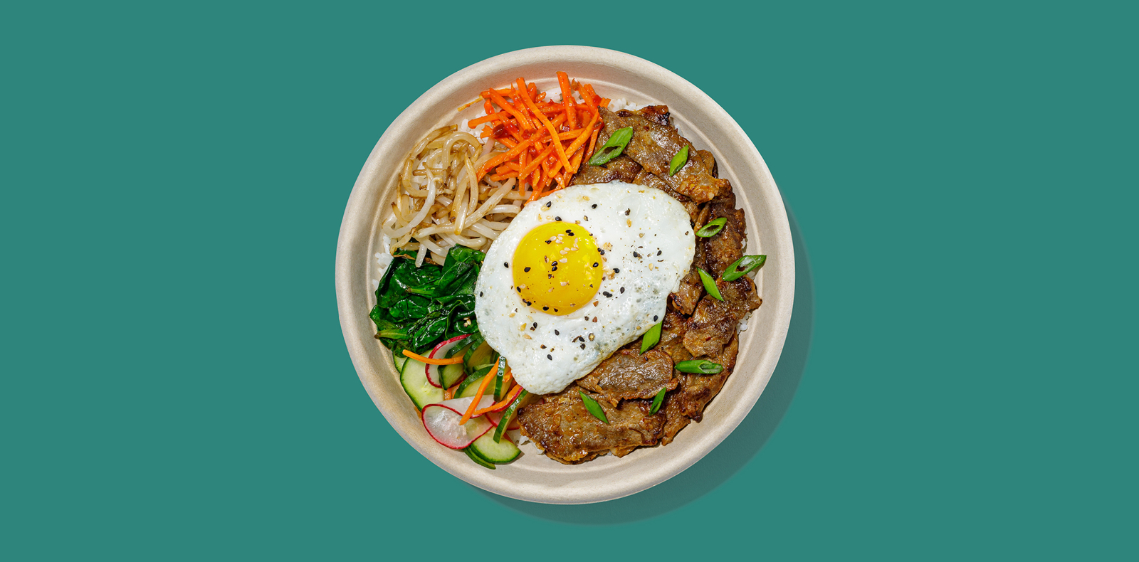 New Roadtrip Bowl called Korean Ribeye Bibimbap with Gochujang-marinated shaved ribeye, steamed rice, spicy carrots, pickled cucumbers, bean sprouts, spinach, sesame seeds, green onions, sunny-side up egg alt tag 